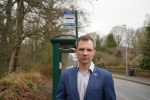 Andrew Bowie standing by a bus stop.